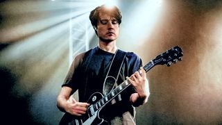 A photo of Jack Moore, son of guitarist Gary Moore, playing a Gibson Les Paul guitar under a beam of stage lights