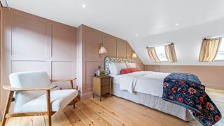 loft bedroom with wooden floor, pale pink panelled walls, bed, chair and velux windows