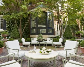 A garden with outdoor seating area, sage green and white furniture and Japanese maples