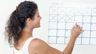 A woman crosses off day on the January page of a calendar