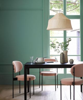 Green painted dining room with pink velvet chairs and black table