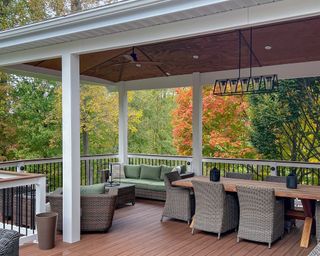 A luxury elevated deck with wicker patio furniture, wood dining table with chairs, ceiling fan and modern chandelier. Pictured in autumn with fall colors.