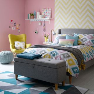 bedroom with pink and yellow designed wall grey bed with designed cushion and wooden flooring