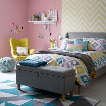 bedroom with pink and yellow designed wall grey bed with designed cushion and wooden flooring
