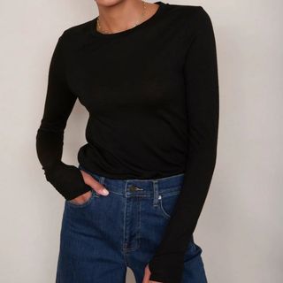 A model wears a black long sleeve tee with jeans. She's standing against a neutral coloured wall