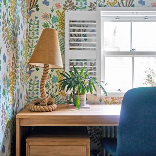 wooden desk with plant and lamp in front of bright patterned wallpaper