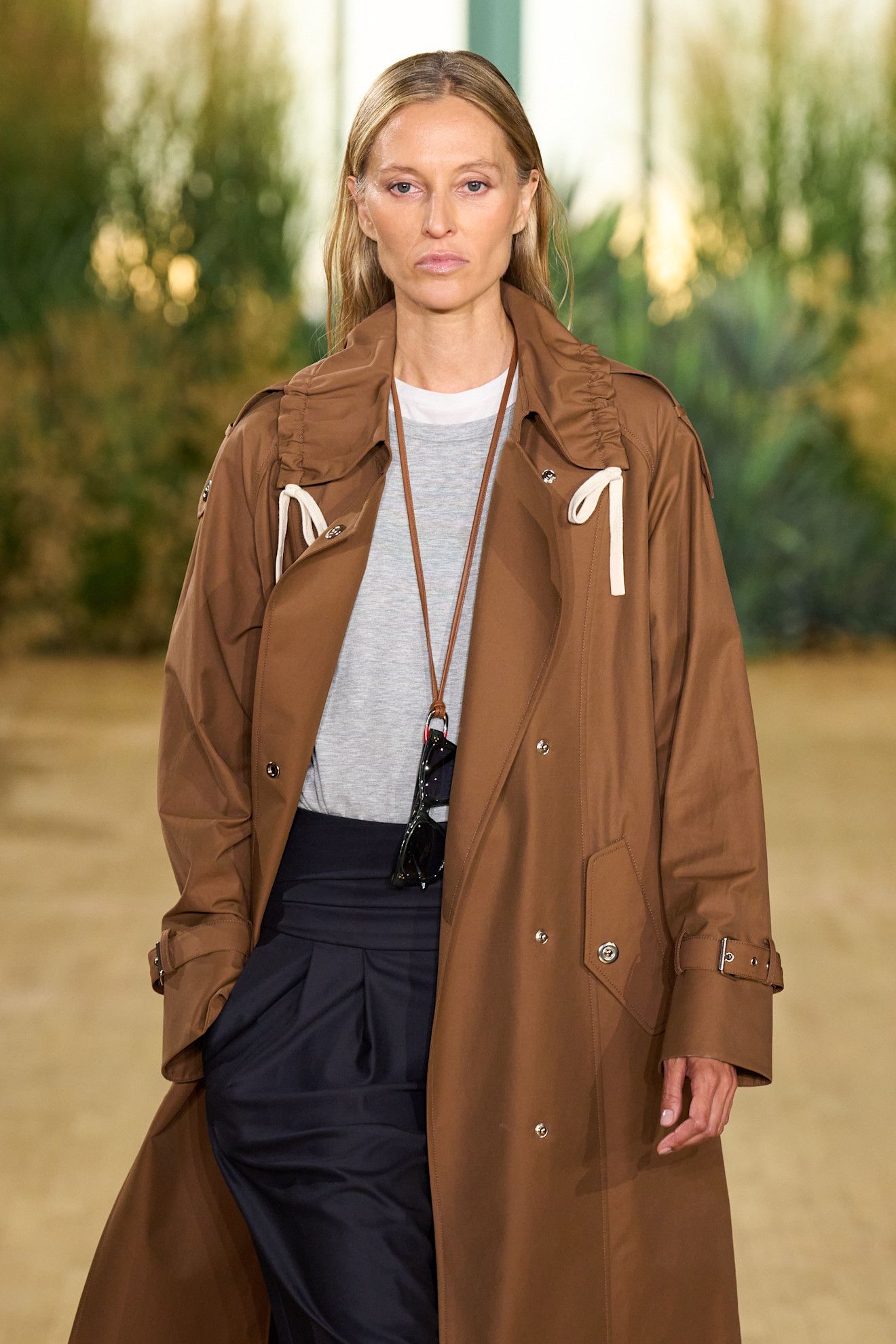 a model walking down the runway at theTWP S27 show wearing a camel trench and grey sweater