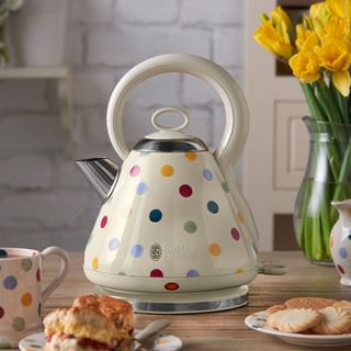polka dot printed white kettle on wooden table with daffodils in vase