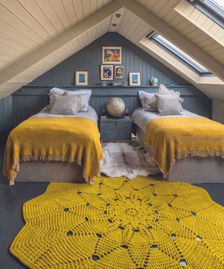 Children's bedroom in the attic with twin beds with mustard yellow throws and rug.