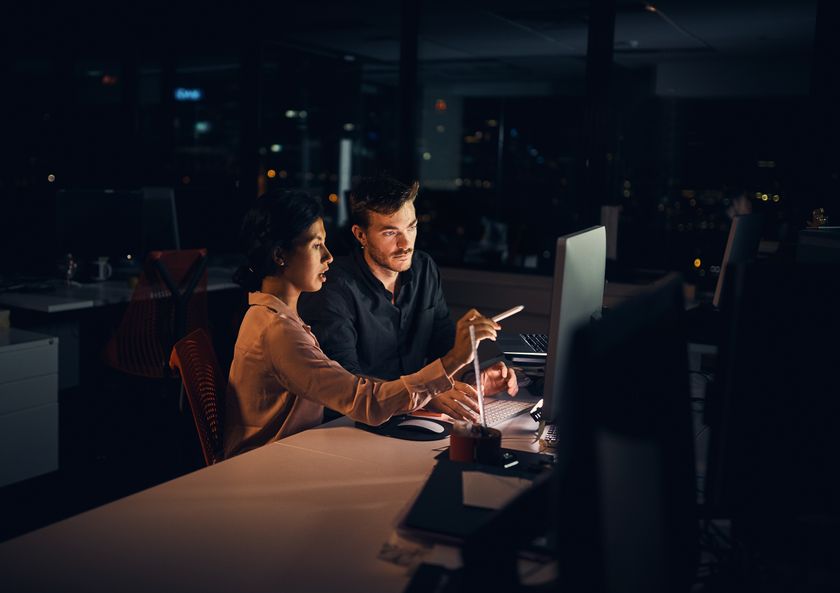 Co-workers talking and pointing at a screen in an office at night