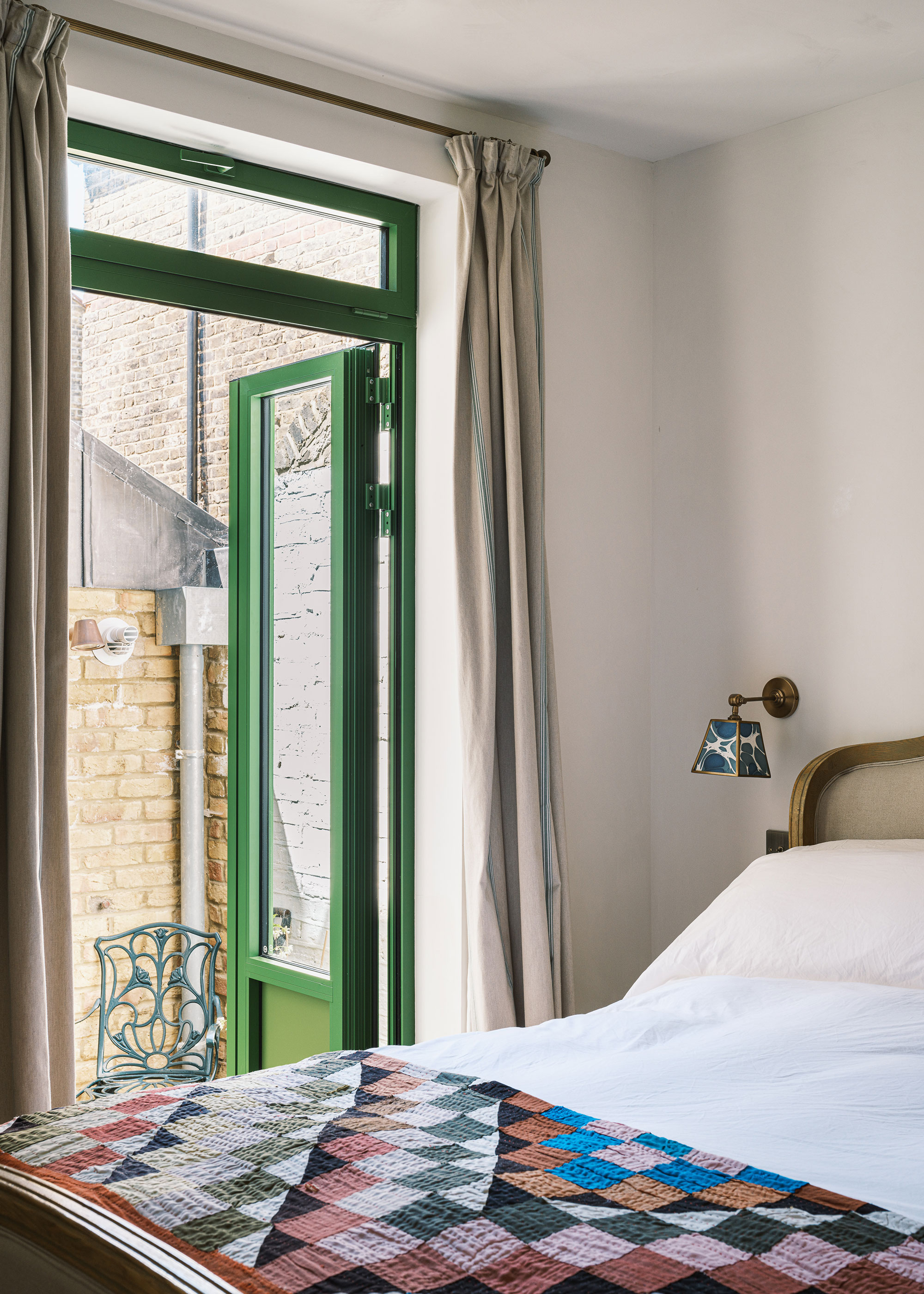 white bedroom with green painted French doors and patchwork quilt