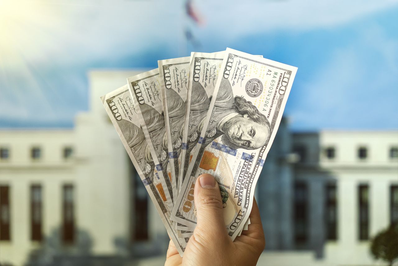 Dollars in a man&#039;s hand held in front of the Federal Reserve Building in Washington DC.