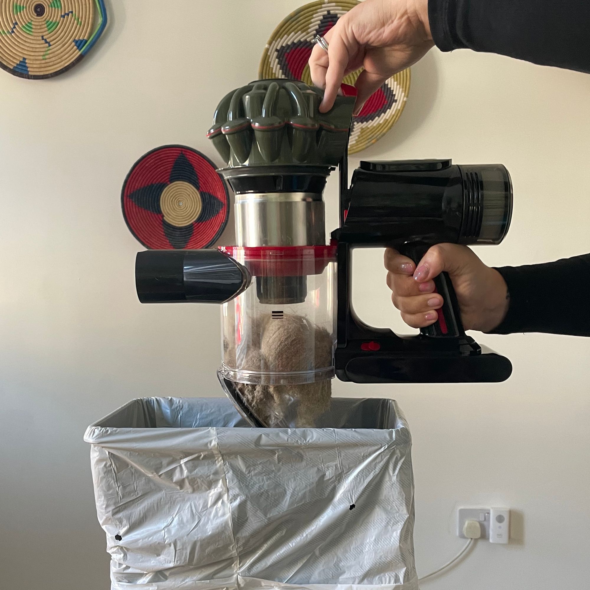 Hand emptying the Dyson V8 Cyclone dust bin over a small bin with a bin bag inside of it