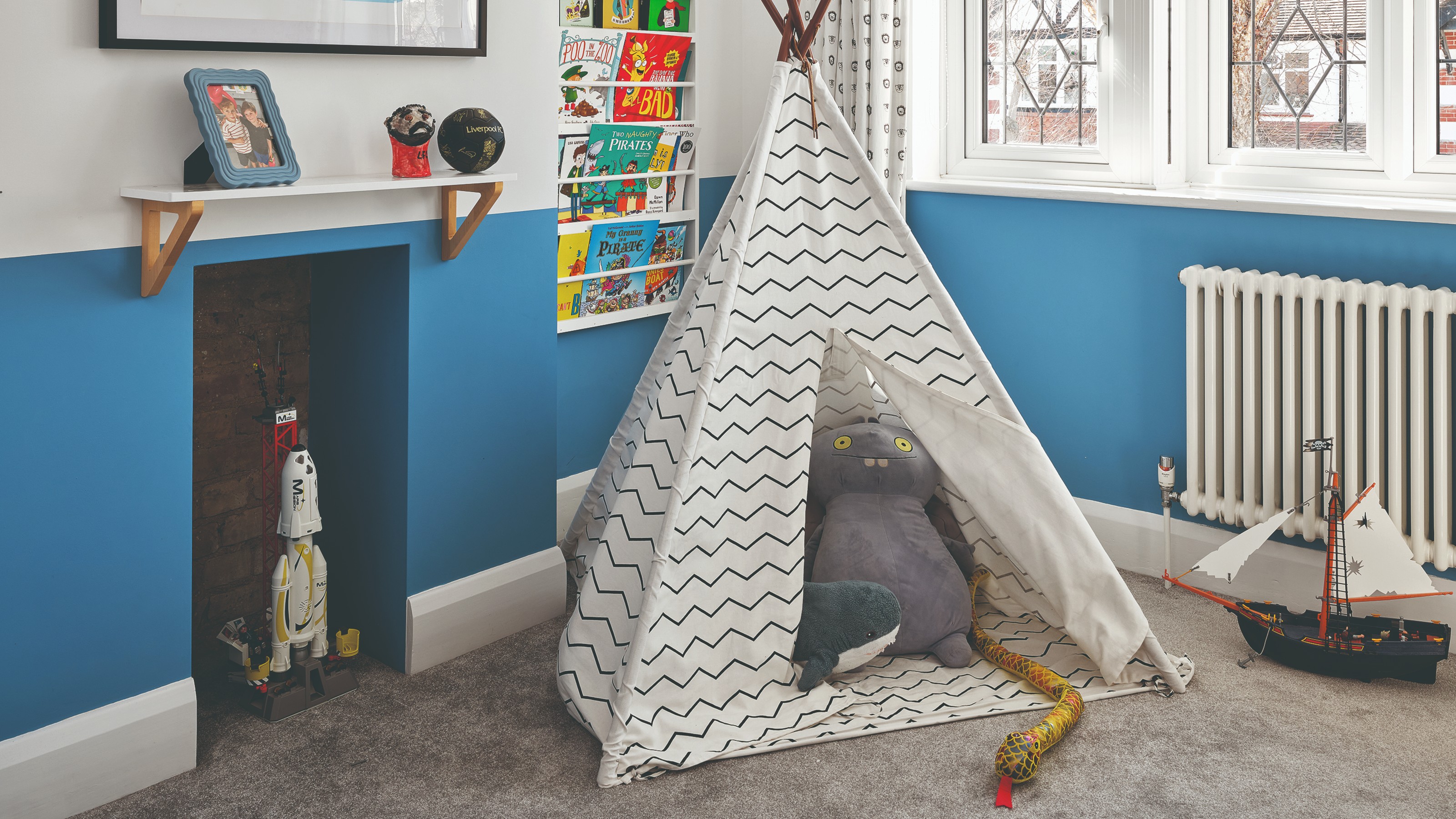 A playroom with a teepee tent in the middle, a book display on the wall and half of the wall painted blue