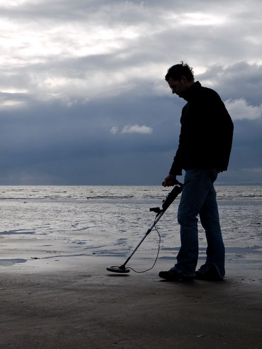 A man using a metal detector on a beach.