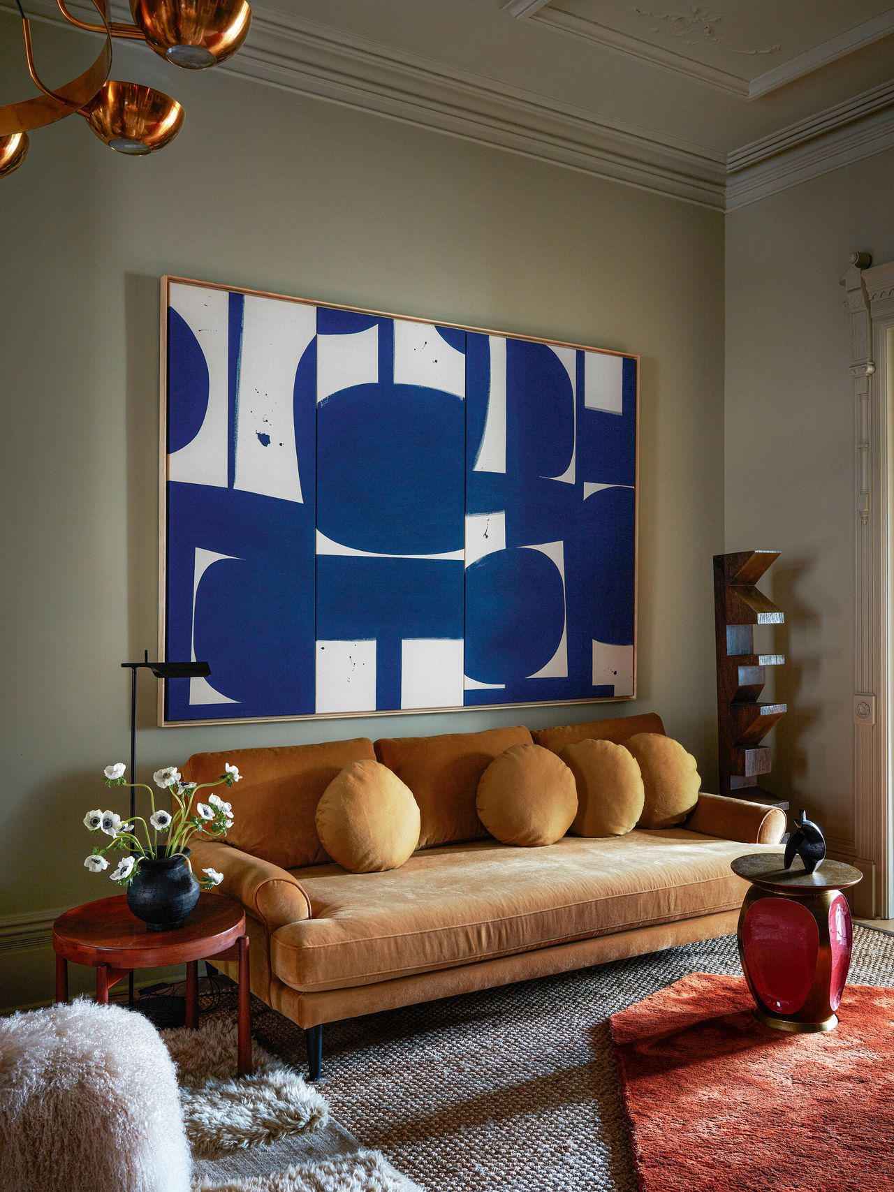 A blue painting hanging above an orange-toned velvet sofa with red accent details around