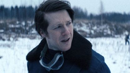 A man stands in a snowy field looking over his shoulder