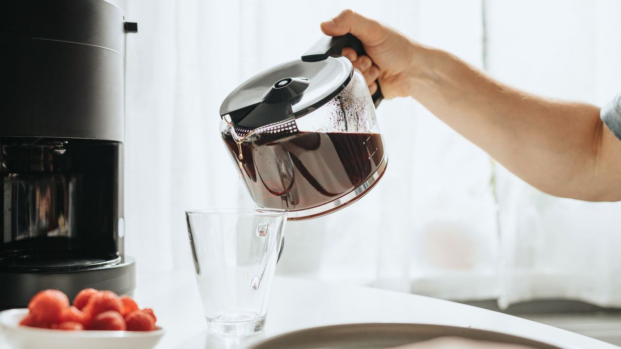 How to make drip coffee at home. A hand pouring drip coffee from a carafe with the drip coffee maker in the background