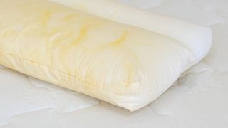 A white pillow with lots of yellow stains resting on a white mattress