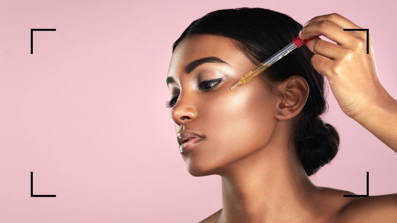 Studio shot of a woman applying coconut oil on the face with a dropper posing against a pink background