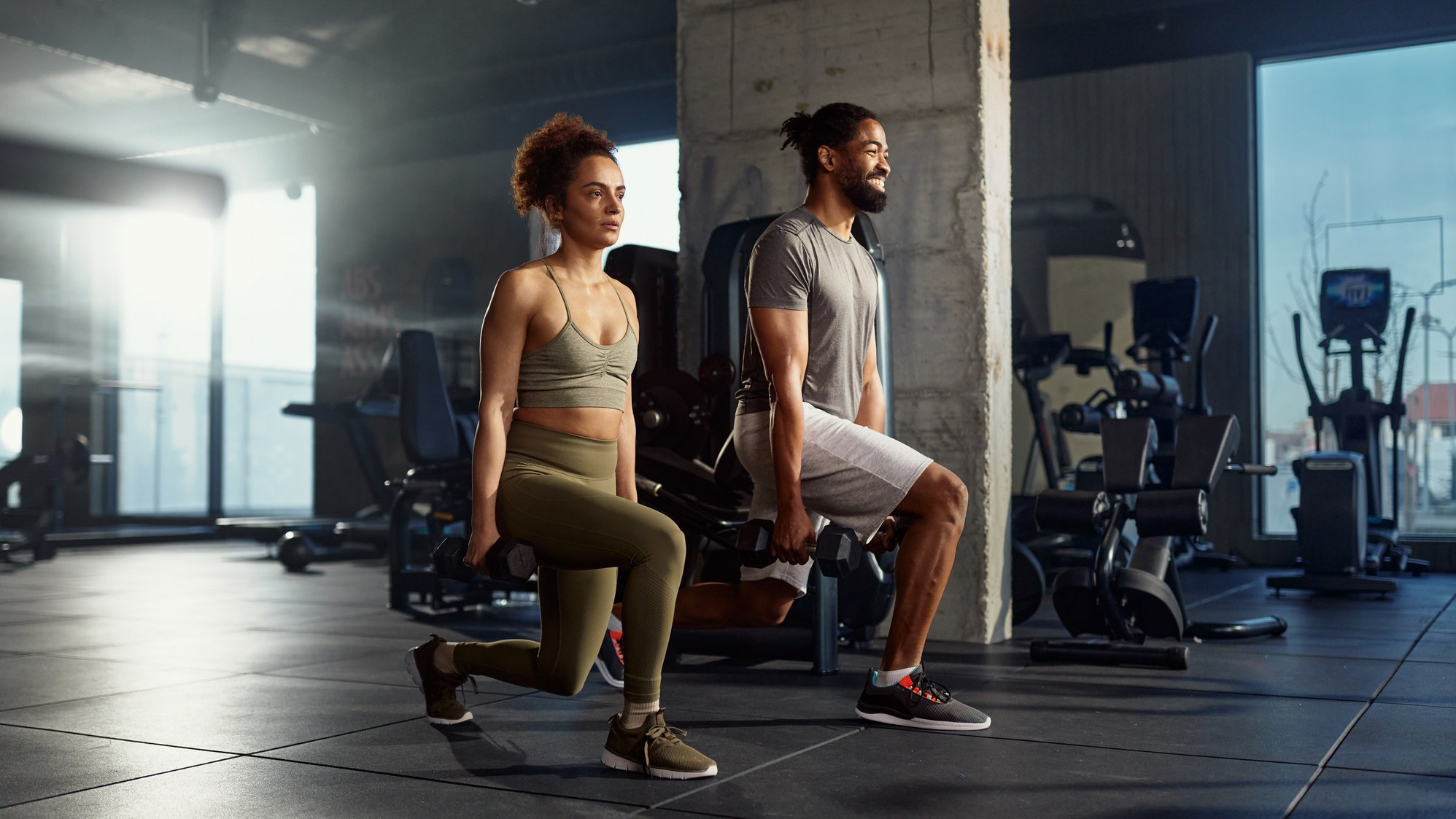 Man and woman in gym, lunging with dumbbells