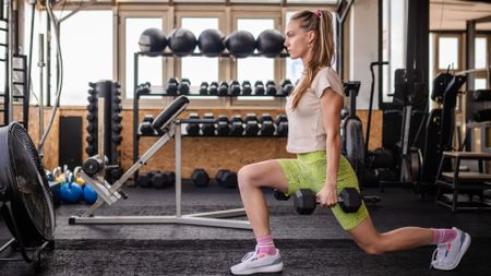 A woman doing dumbbell lunges at the gym