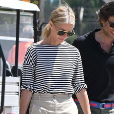 Gwyneth Paltrow wearing a striped tee with khaki pants, a Goyard tote, and ankle-wrap sandals in Sardinia