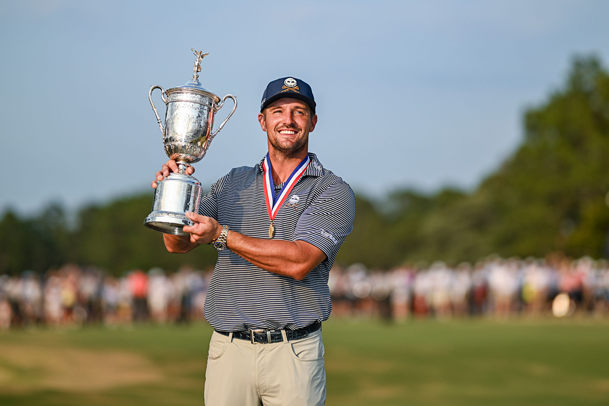 Bryson DeChambeau wearing a winners medal, holding the US Open trophy aloft after winning the Major Championship in 2024 at Pinehurst No.2