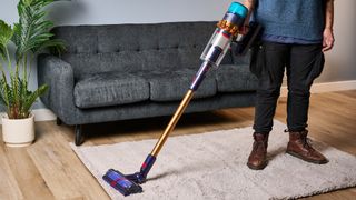 the dyson gen5detect cordless stick vacuum in prussian blue and copper, showing its cleaning head and attachment tools