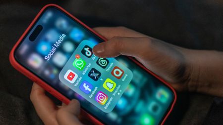 A 12-year-old boy looks at an iPhone screen showing various social media apps including TikTok, Facebook and X,