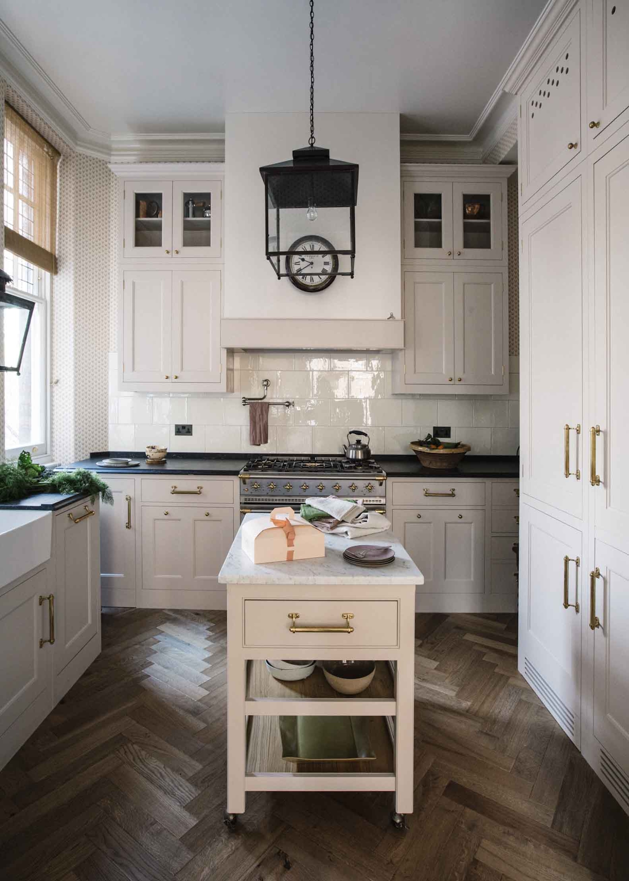 a small white kitchen with a small island in the middle. The island has extra storage space with a drawer as well as open shelving. A pendant light hangs above the island.