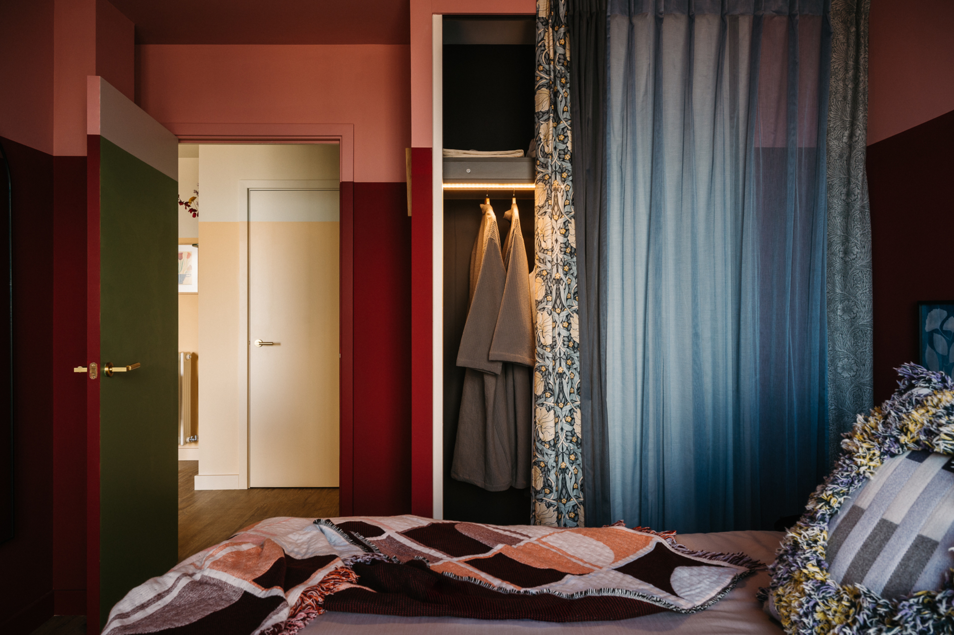 Bedroom with green, pink and red walls, blue curtains covering wardrobe