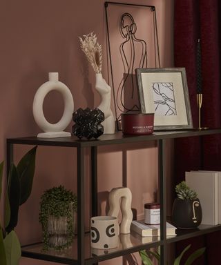 A living room with dark red wall paint decor and black shelving with candles and other ornamental decor