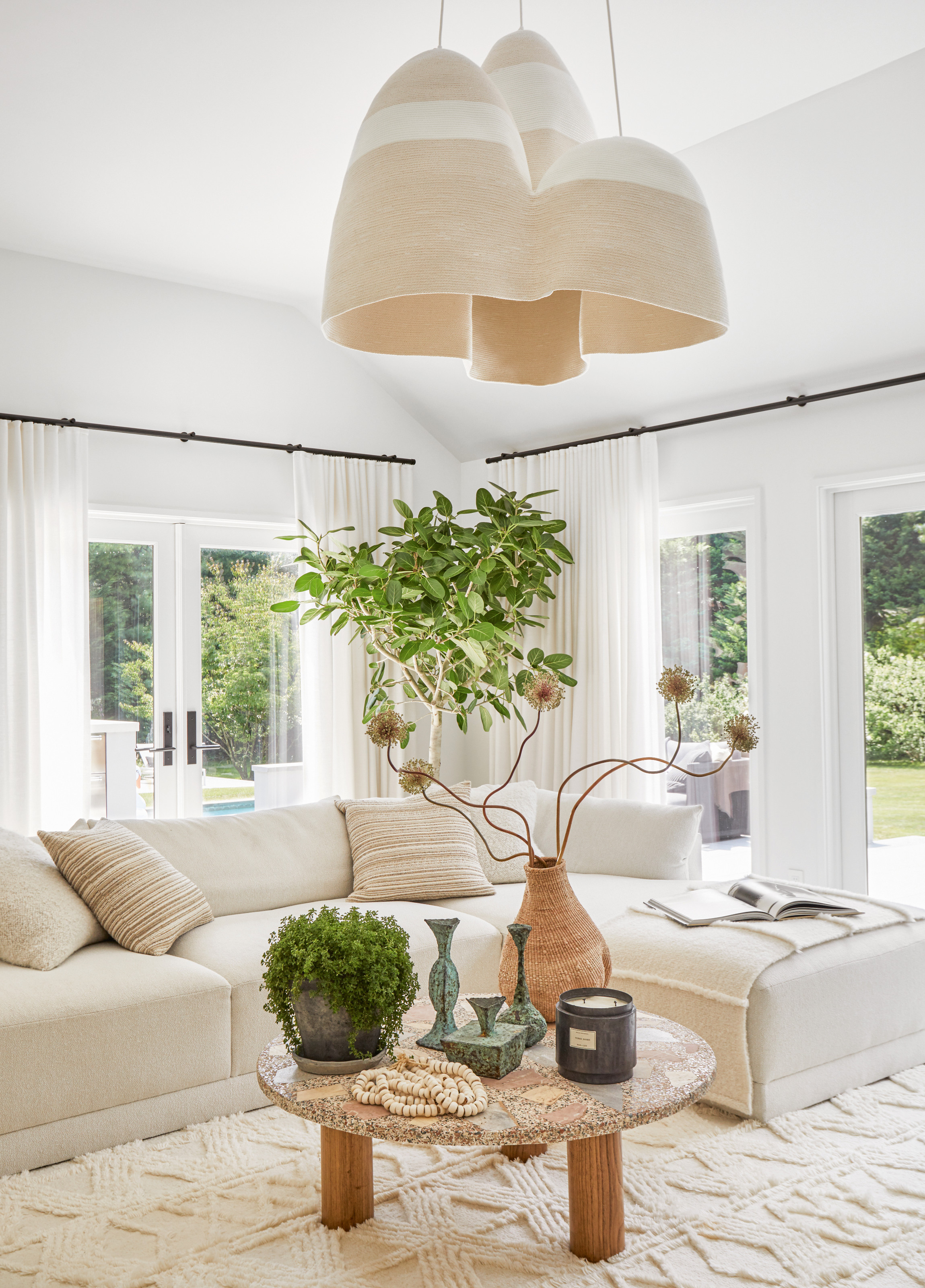 White living room with white chaise sofa, terrazzo top coffee table, trio of suspended lights and an indoor tree