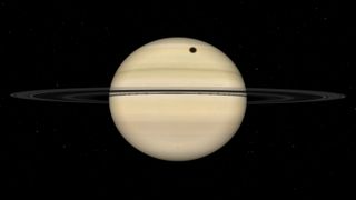 A simulation of the gas giant Saturn fully illuminated by direct sunlight. The planet's sweeping rings are positioned almost edge on to the observer, and a dark circular shadow is visible on the banded cloud surface above the ring line.