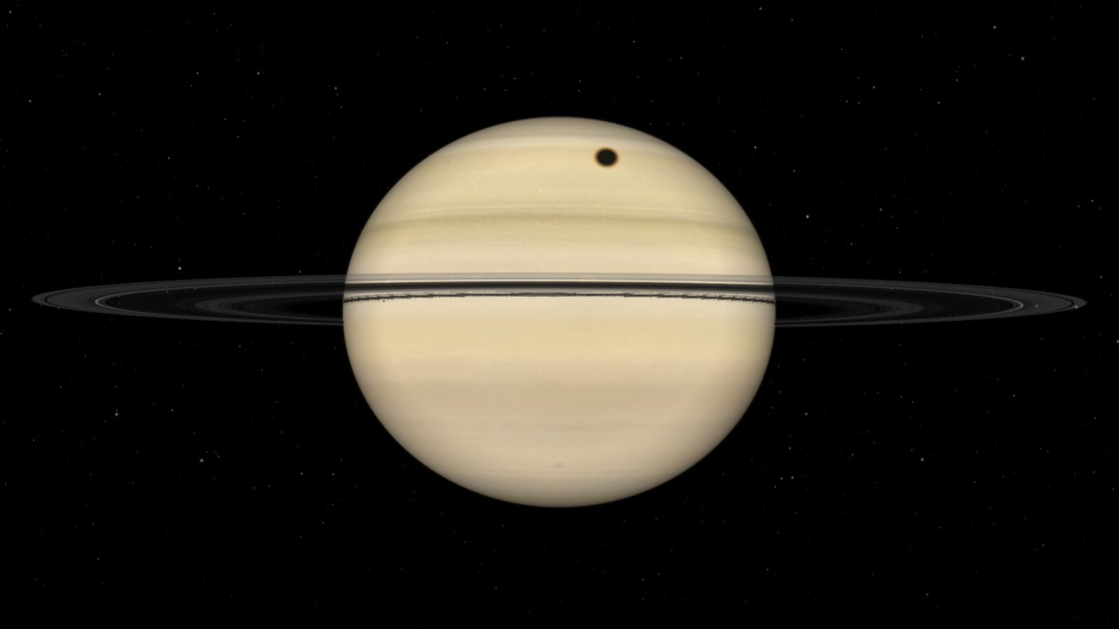 A simulation of the gas giant Saturn fully illuminated by direct sunlight. The planet&#039;s sweeping rings are positioned almost edge on to the observer, and a dark circular shadow is visible on the banded cloud surface above the ring line.