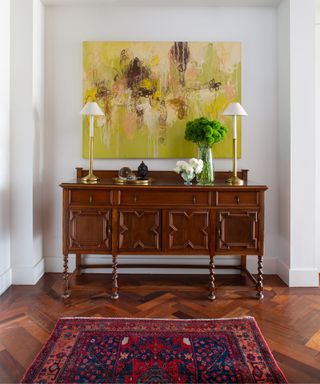 entryway with white walls, parquet floor, wooden dresser with yellow abstract artwork above