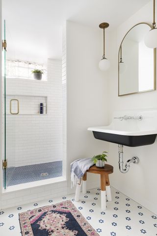 white bathroom with vintage sink, retro mirror and wall lights, stool, walk in shower and vintage rug