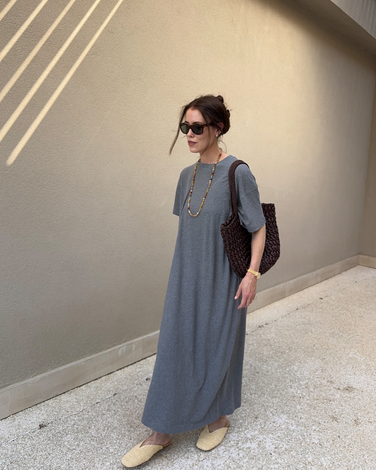 Woman wears grey T-shirt dress, woven mules and carries brown woven bag