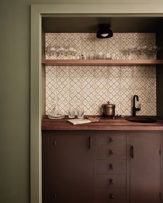 A sage green kitchen with earthy brown cabinets and wooden worktops and patterned tiles for a splashback