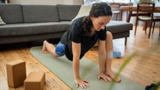 Woman stretches her hips in front of a couch with two yoga blocks to the side of her
