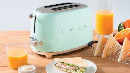 A light blue Smeg 50s Retro 2 Slice Toaster with toast, a sandwich, and orange juice