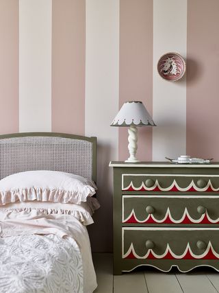 Pink and white striped wall with bed and green set of drawers with white and red painted design