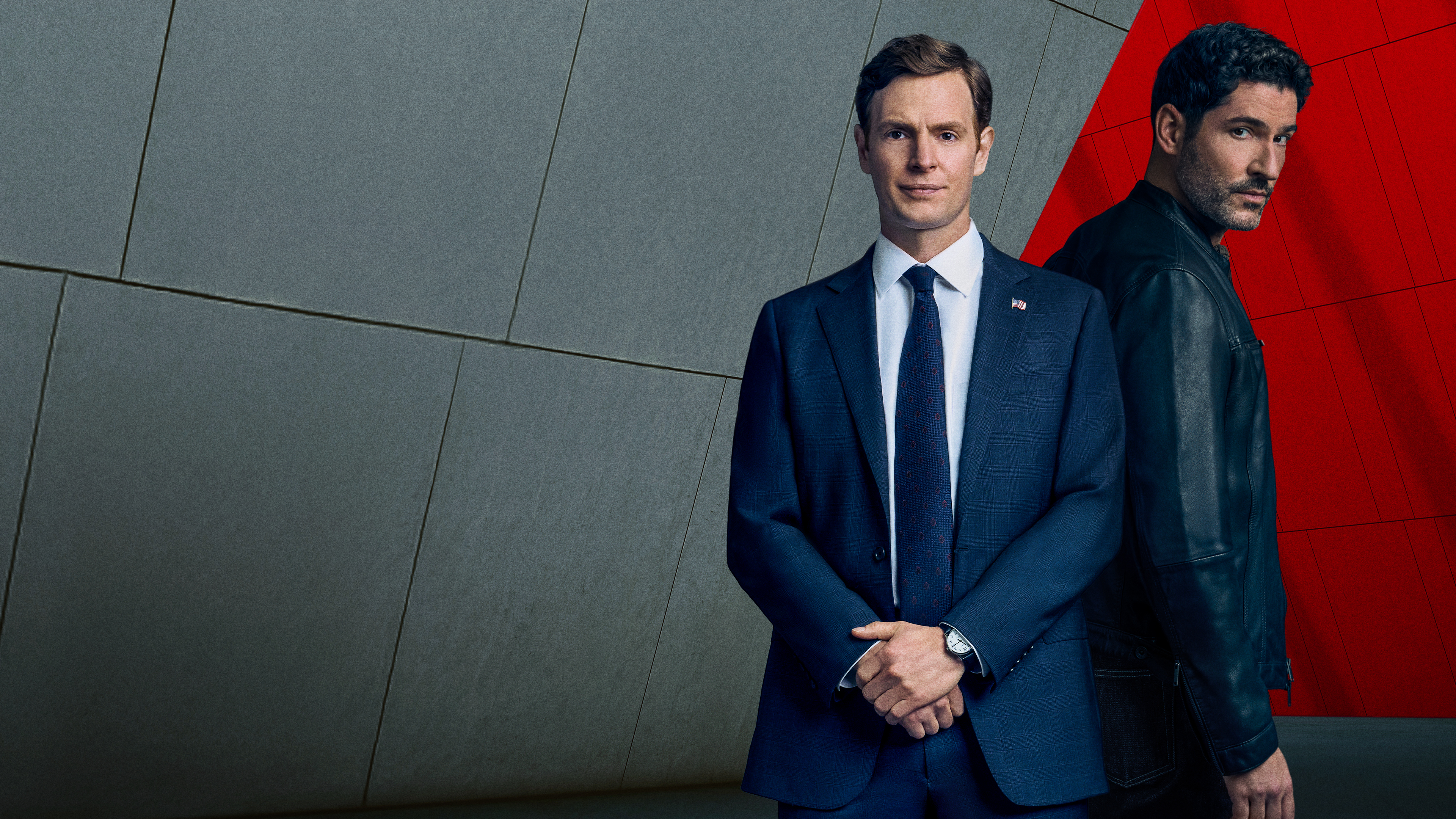 CIA key art. Nick Gehlfuss as Bill Goodman and Tom Ellis as Colin Glass. Bill stands in front of a grey background wearing a suit and Colin stands behind him in front of a red background.