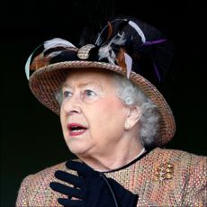Queen Elizabeth looks shocked while wearing black gloves and a large embroidered hat