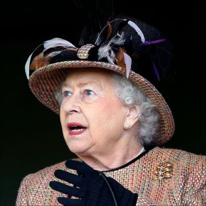 Queen Elizabeth looks shocked while wearing black gloves and a large embroidered hat