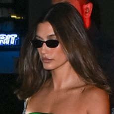 Hailey Bieber wears black sunglasses and a green minidress.