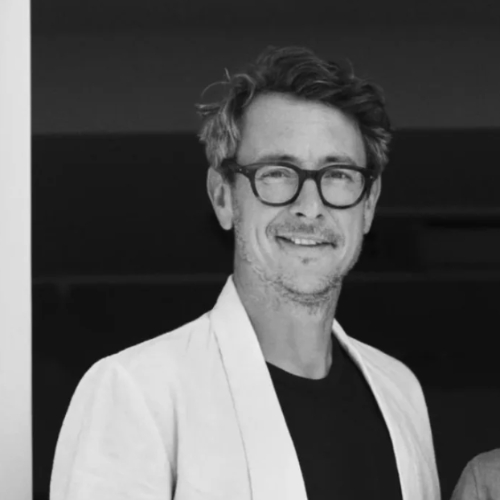 Black and white image of a man in a dark shirt and a white blazer.