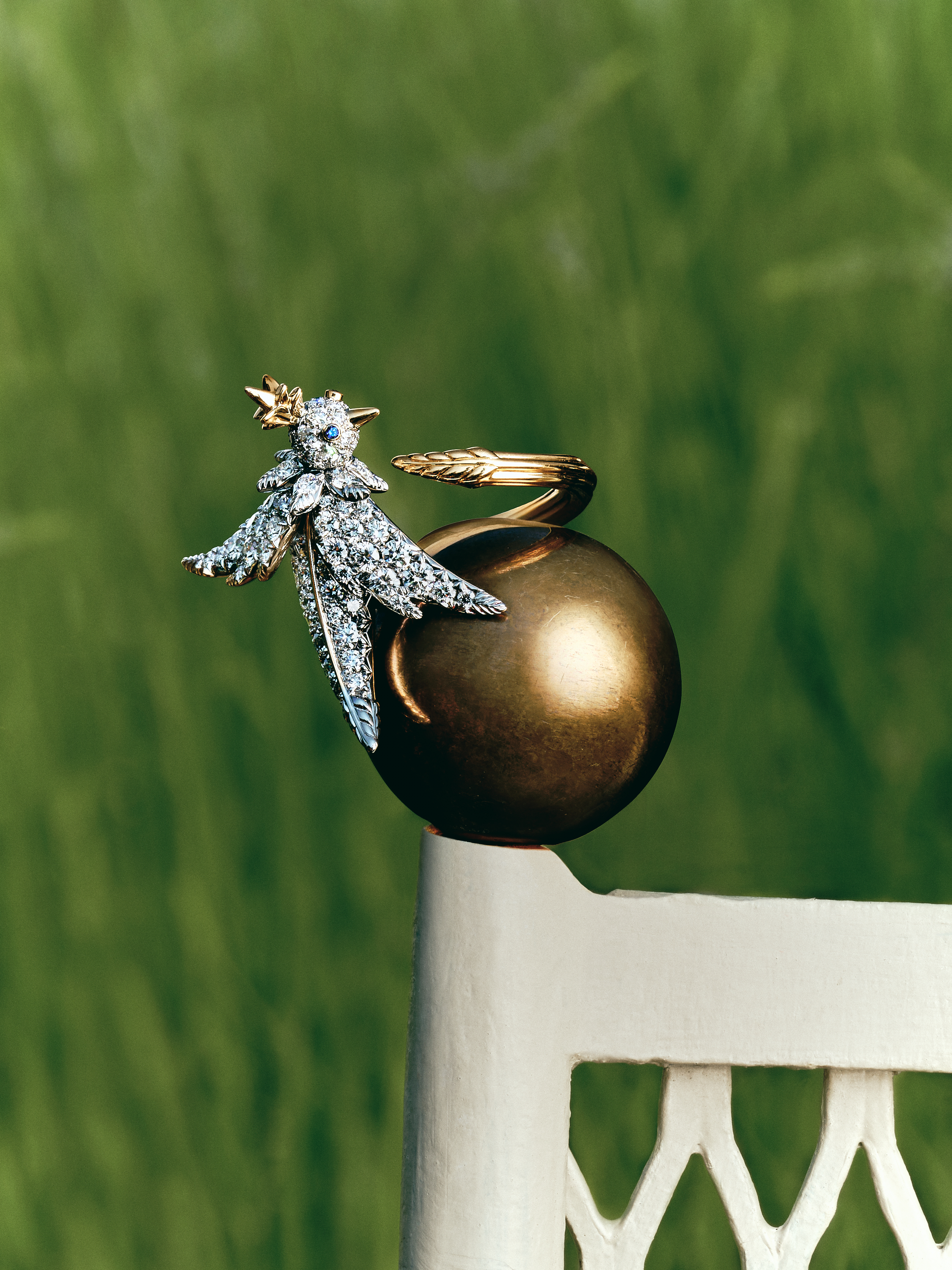 Diamond and gold bird motif ring balanced on the corner of a garden chair