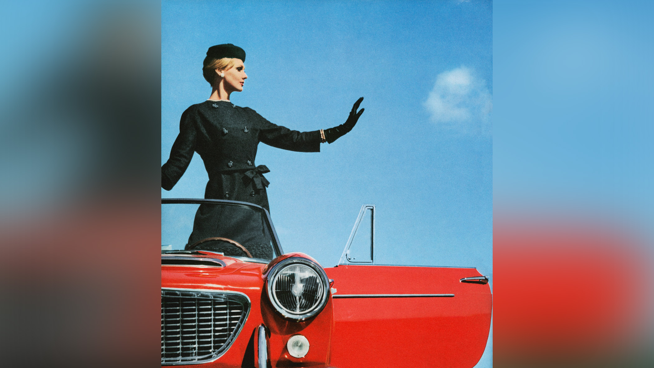  A woman stood in an open-top red car posing. 